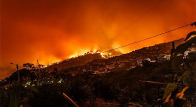 A wildfire engulfs hills near a town, spreading flames and smoke